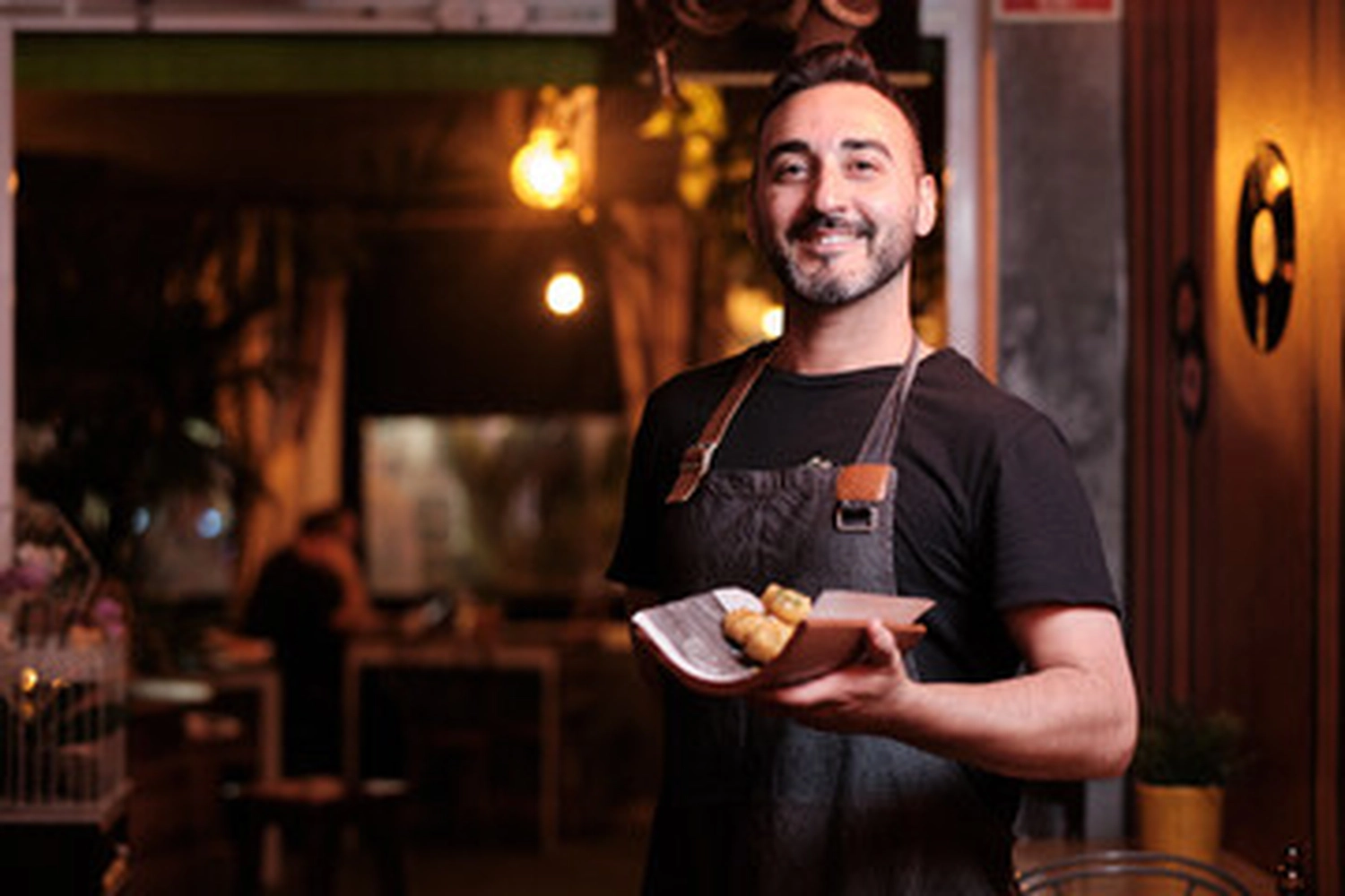 Jobway Germany - Internationale Rekrutierung von Fachkräften - Ein lächelnder Kellner hält in einem Restaurant einen kleinen Teller mit Essen.